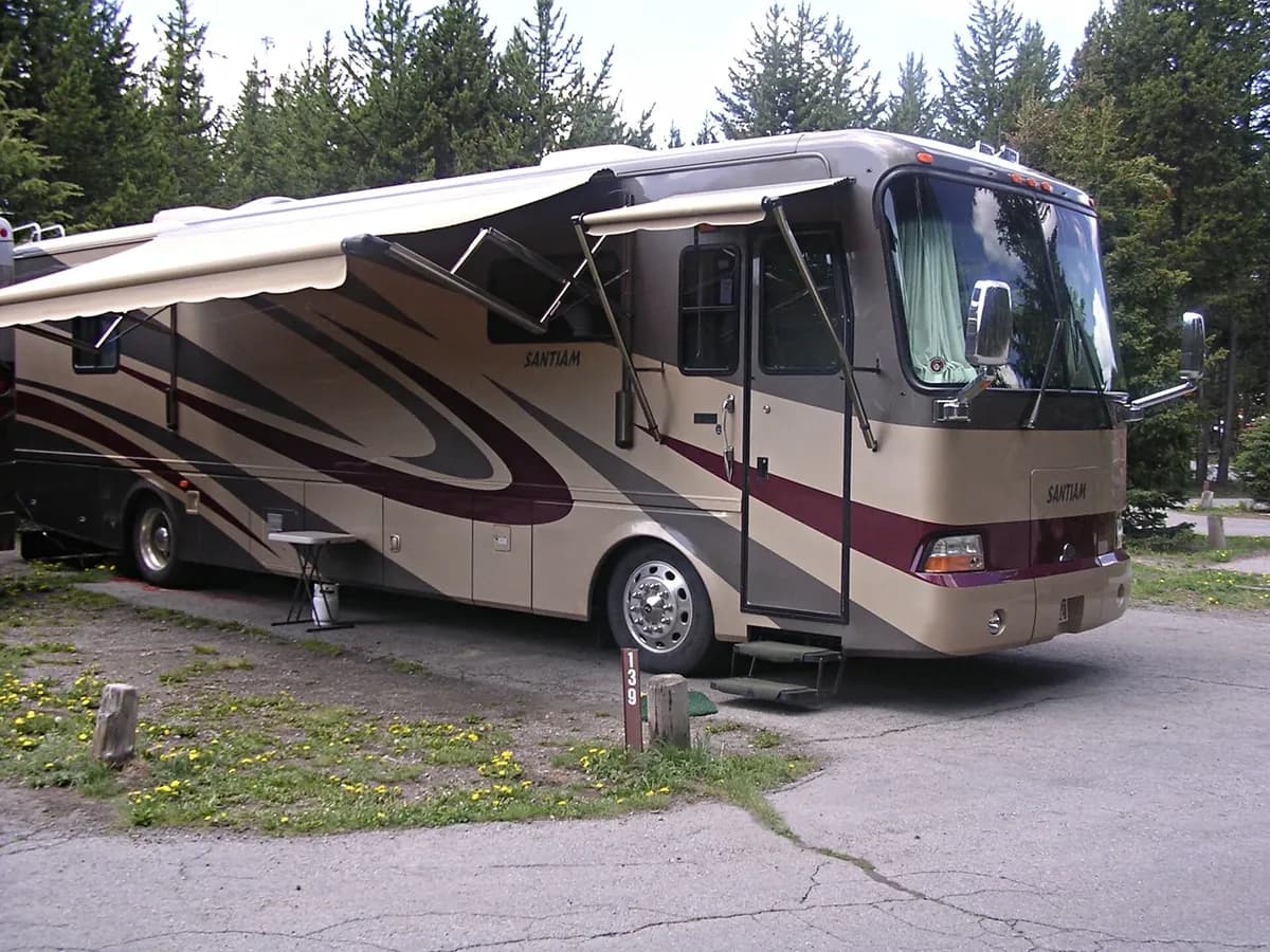 A Class A motorhome with its awning out at a wooded campground