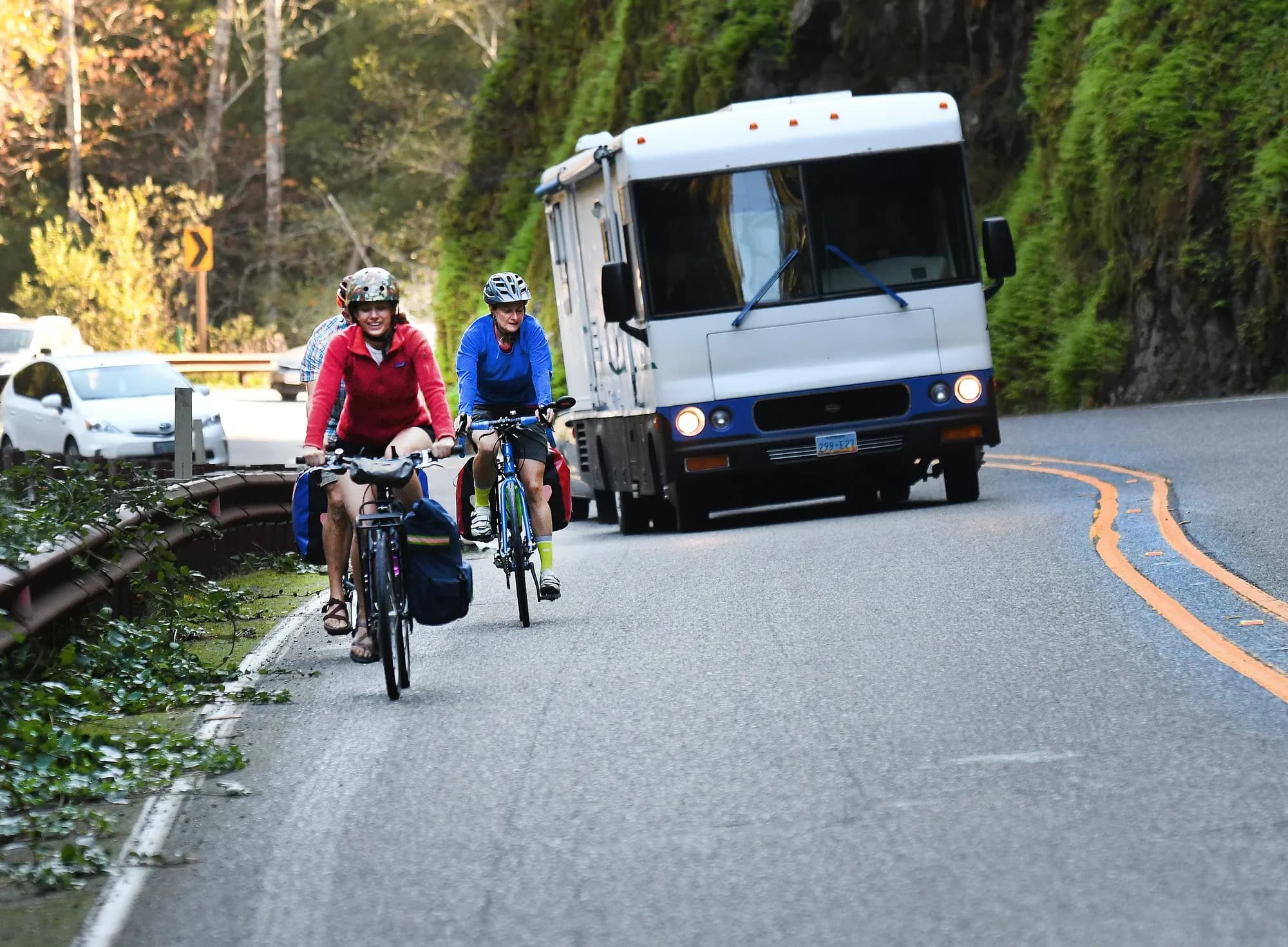 A motorhome sharing a coastal mountain highway with two cyclists