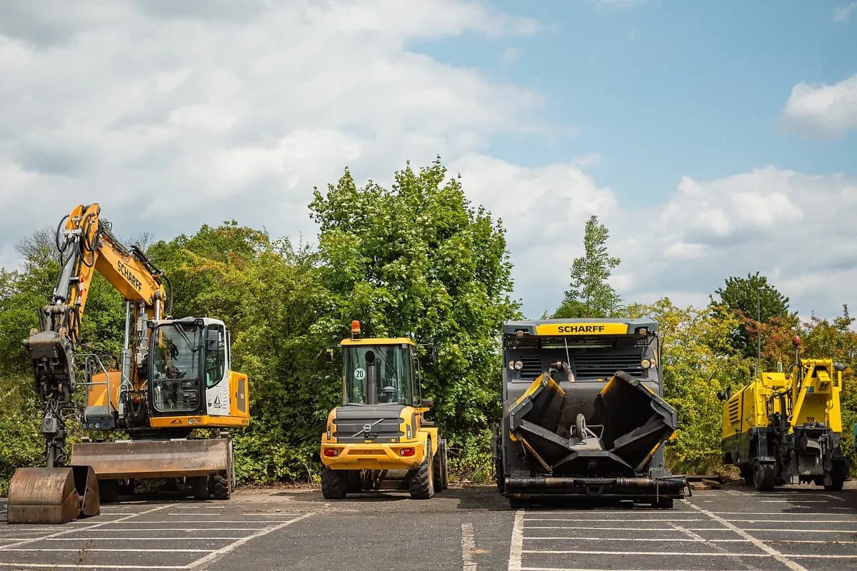 An excavator, roller and sweeper lined up in a contractor's yard